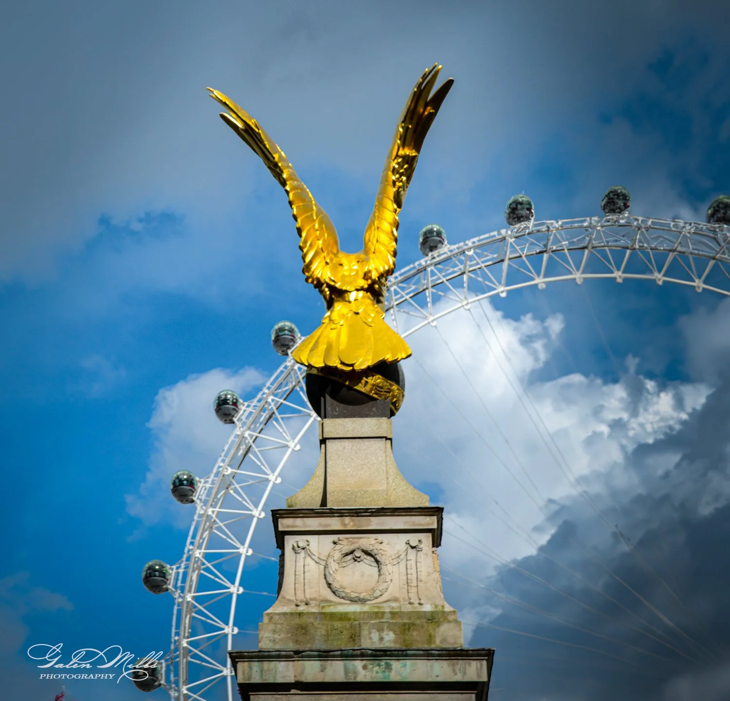 Golden eagle statue atop a stone pedestal with the London Eye in the background against a cloudy sky.