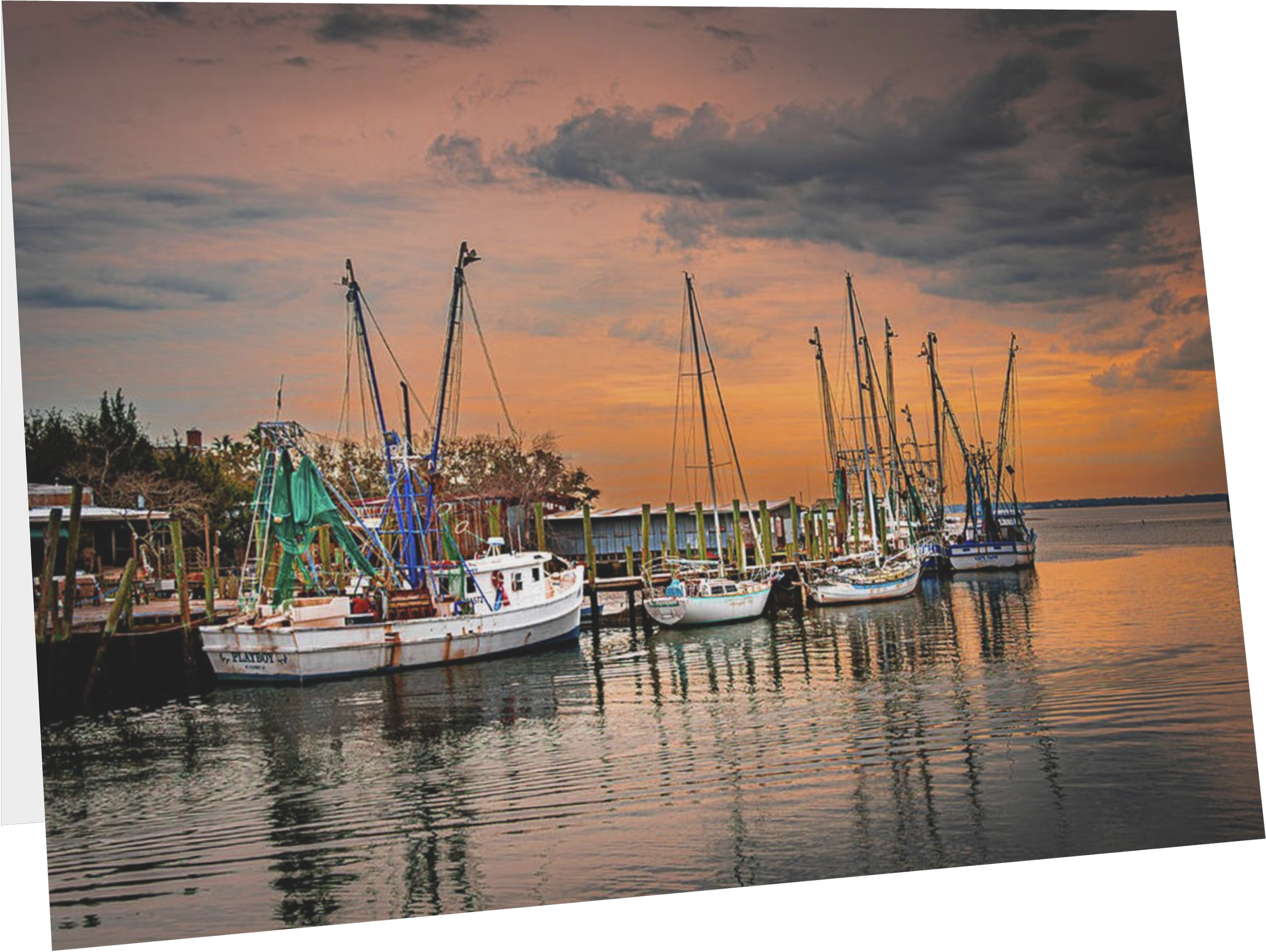 Several sailboats docked at a pier during sunset with a partly cloudy sky reflected in the water.