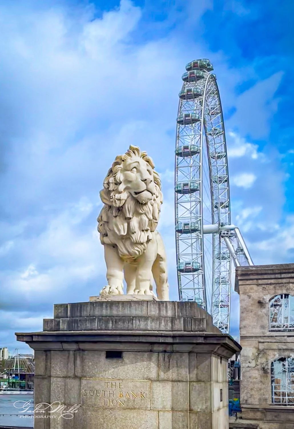 White lion statue, known as the South Bank Lion, in front of a Ferris wheel against a blue sky.