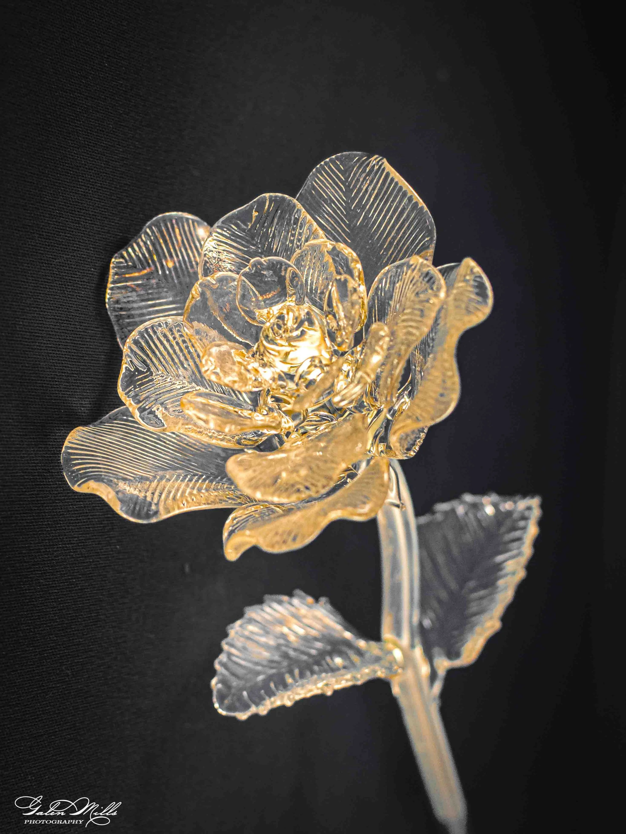 A close-up photo of a crystal floral rose sculpture against a black background, showcasing intricate petal details and clear reflection.