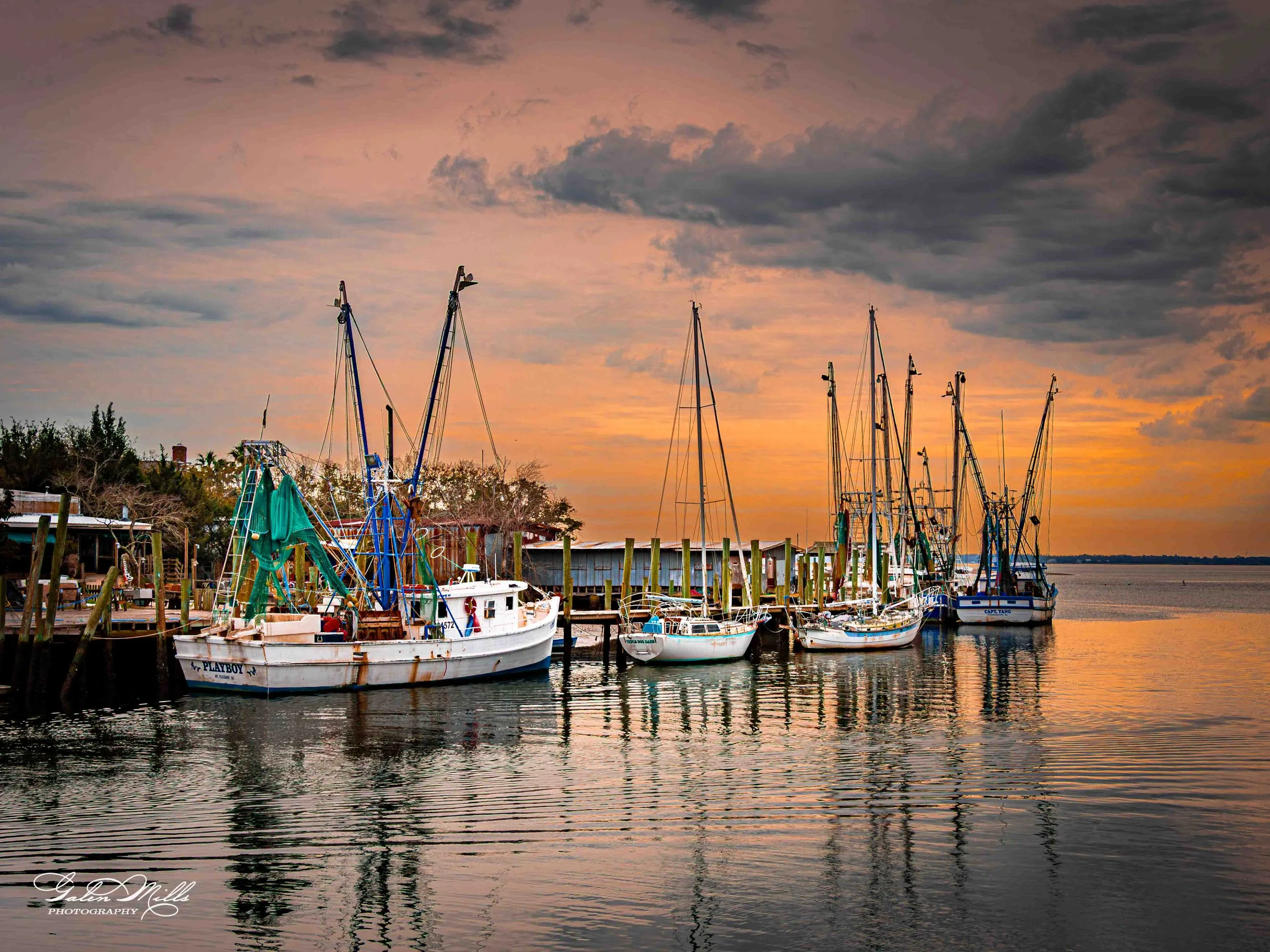 Boats docked at a marina during sunset with a colorful sky and calm water.