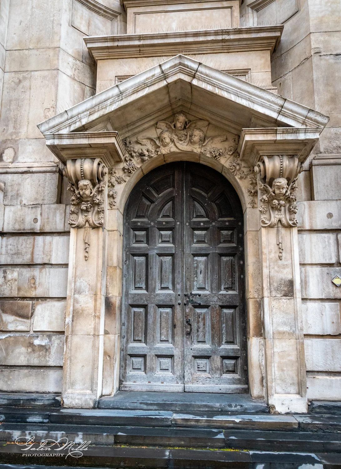 Ornate wooden door with stone carvings and pillars on an old building facade.