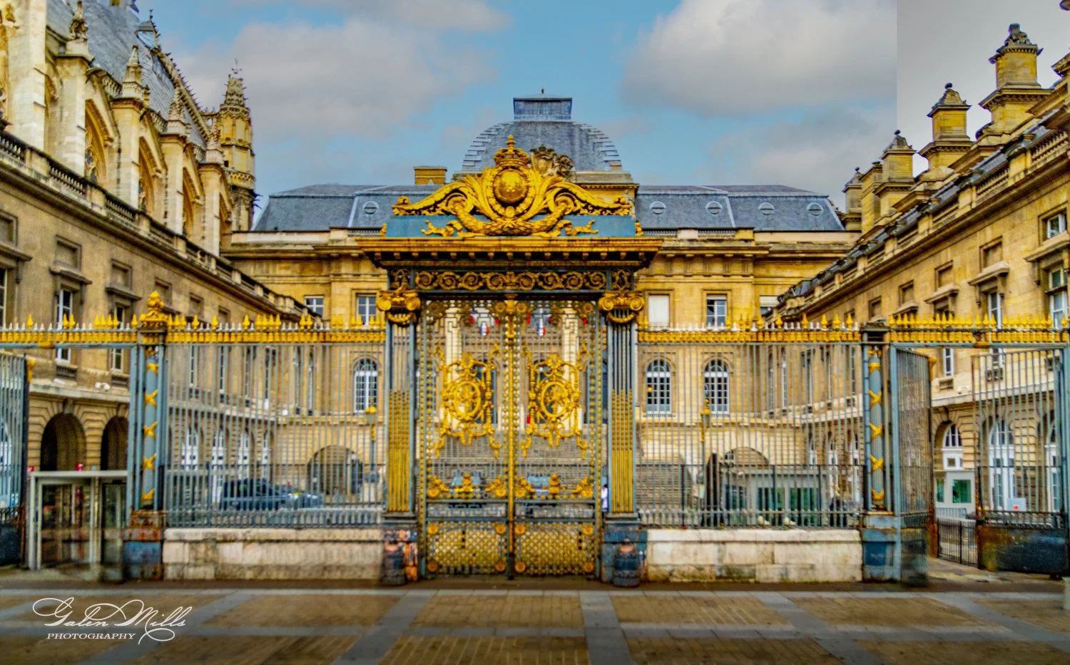 Elaborate golden gate in front of historic stone building with arched windows and decorative architecture.