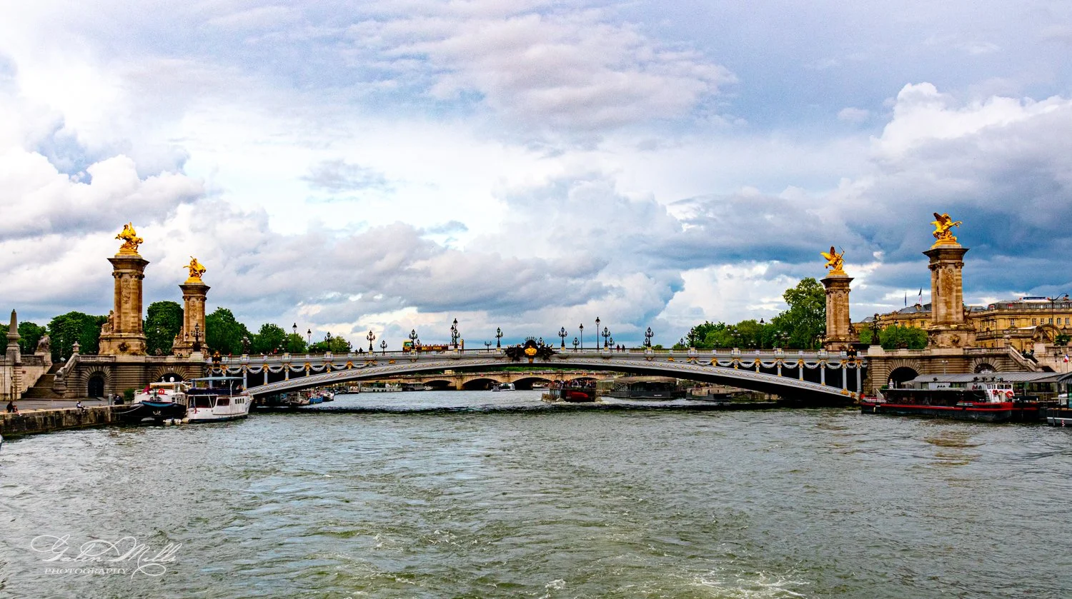 Pont Alexandre III bridge in Paris, adorned with decorative golden sculptures, spanning the Seine River under a cloudy sky.