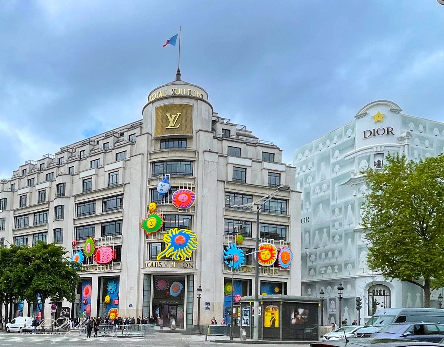 Exterior view of a Louis Vuitton and Dior store in Paris, decorated with colorful, playful designs on the facade under a cloudy sky.