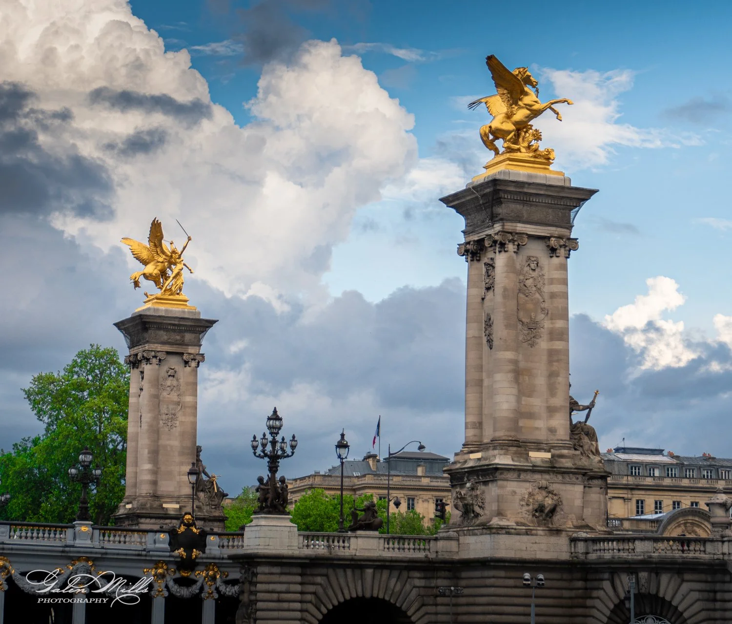 Pont Alexandre III in Paris, featuring ornate golden statues on pillars under a blue sky with clouds.