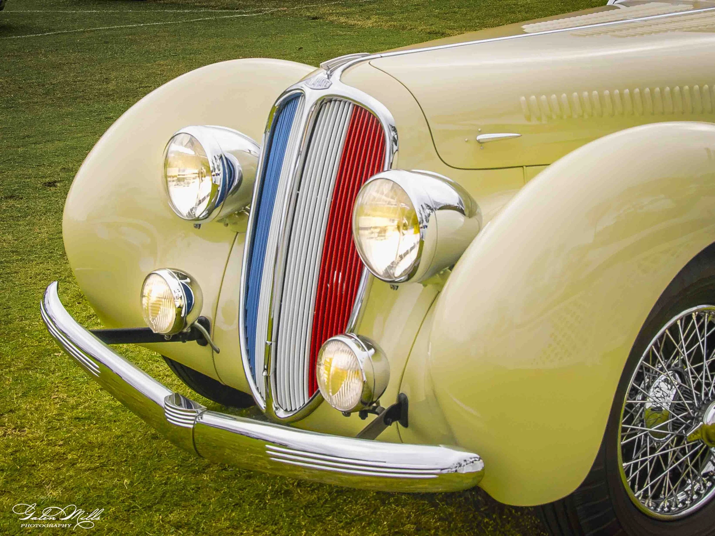 Close-up of a vintage yellow classic car with chrome details and wire wheels, parked on grass.
