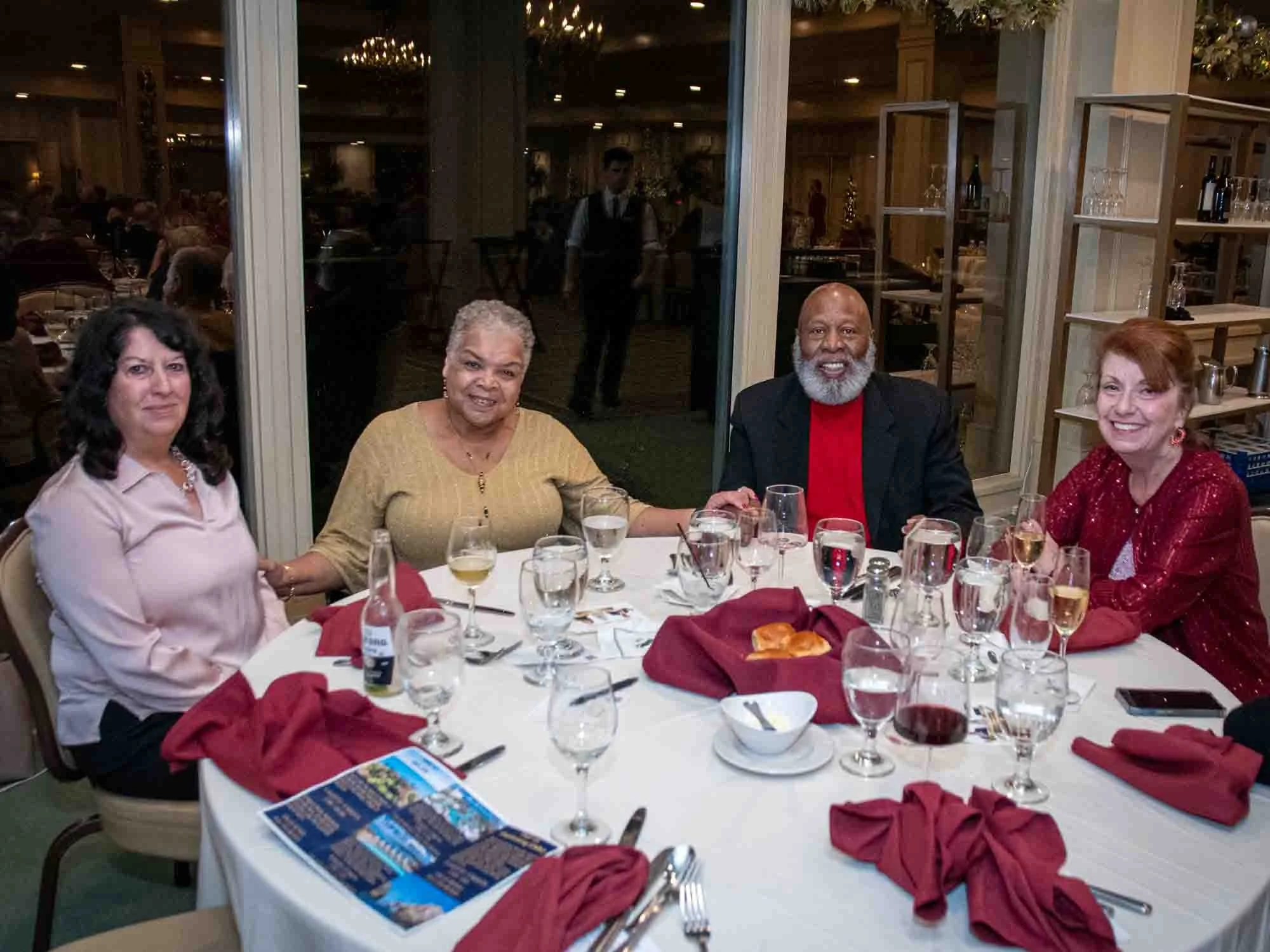 Four people sitting at a round dining table with drinks and red napkins in a restaurant setting.