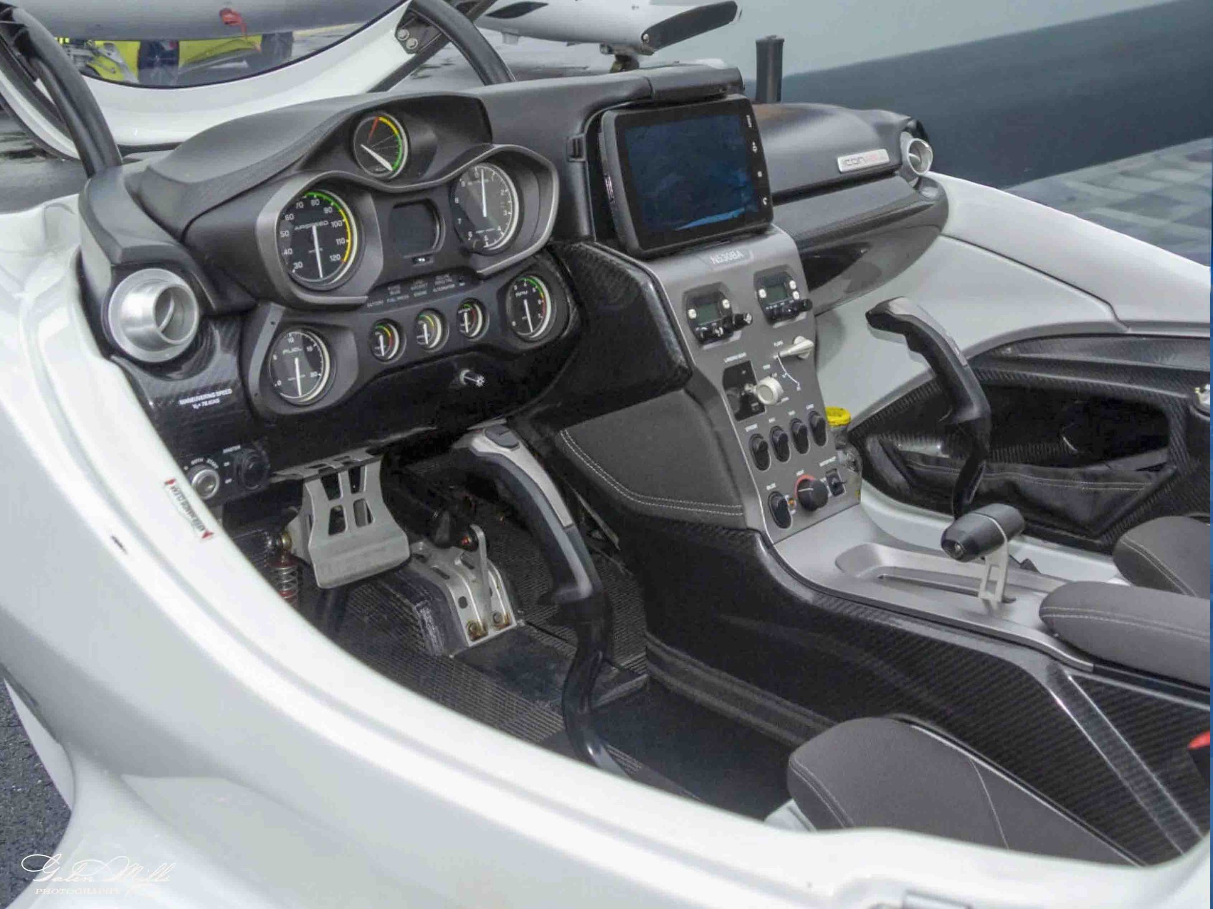 A close-up view of a racing vehicle's cockpit, featuring a dashboard with several gauges, a touchscreen display, and various control switches and knobs.