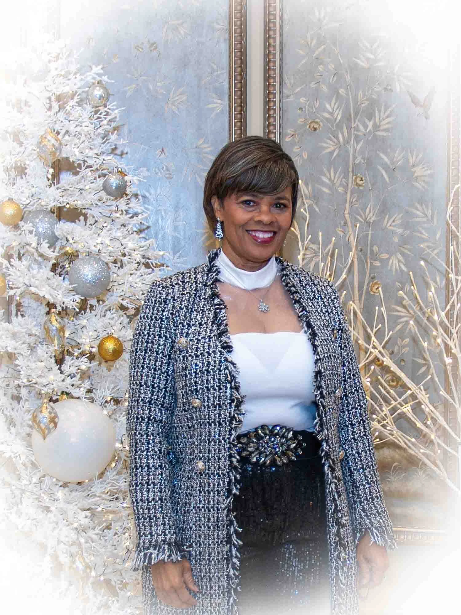 Woman in formal attire standing by a decorated Christmas tree.