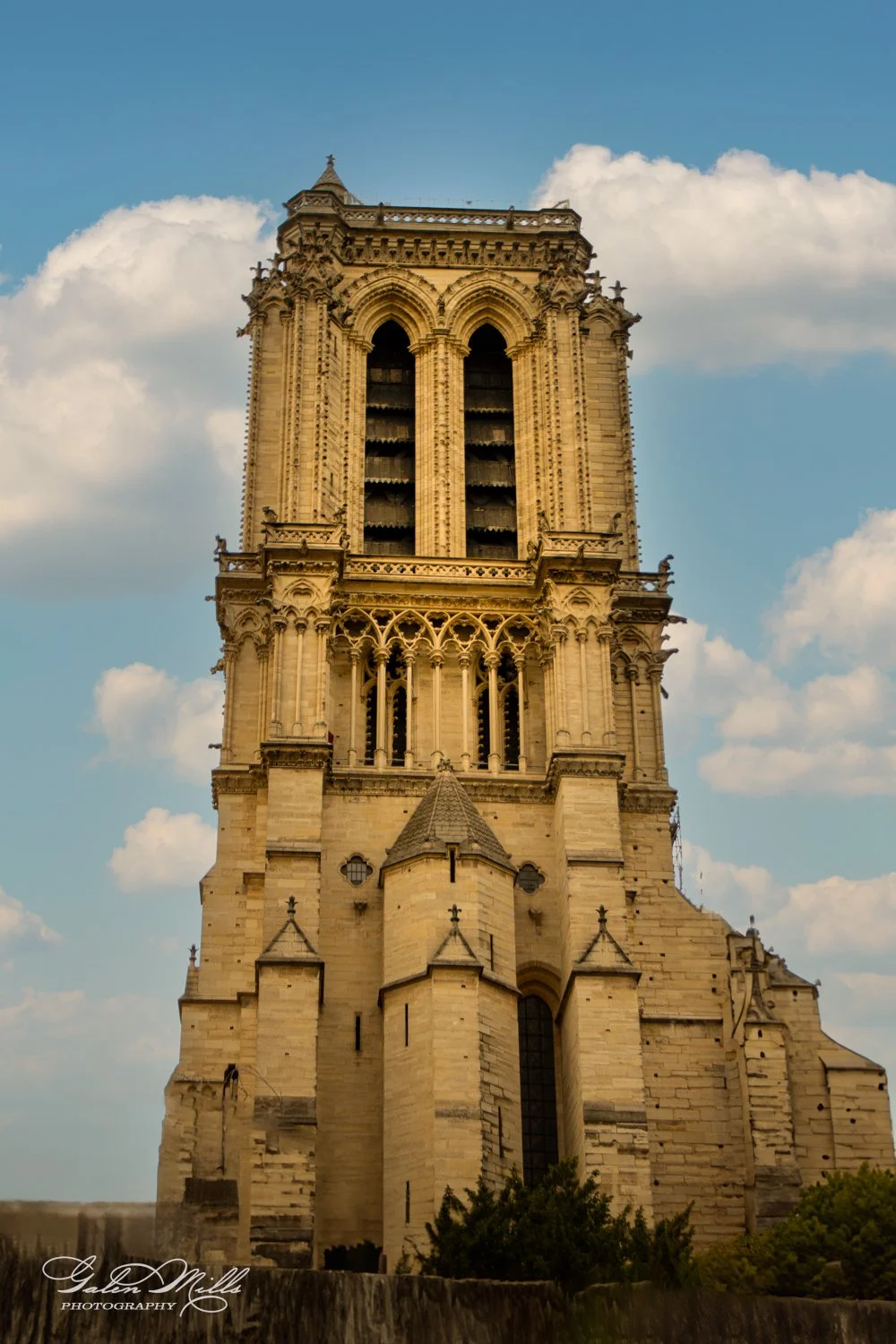 Gothic architecture of Notre-Dame Cathedral tower against blue sky with clouds.