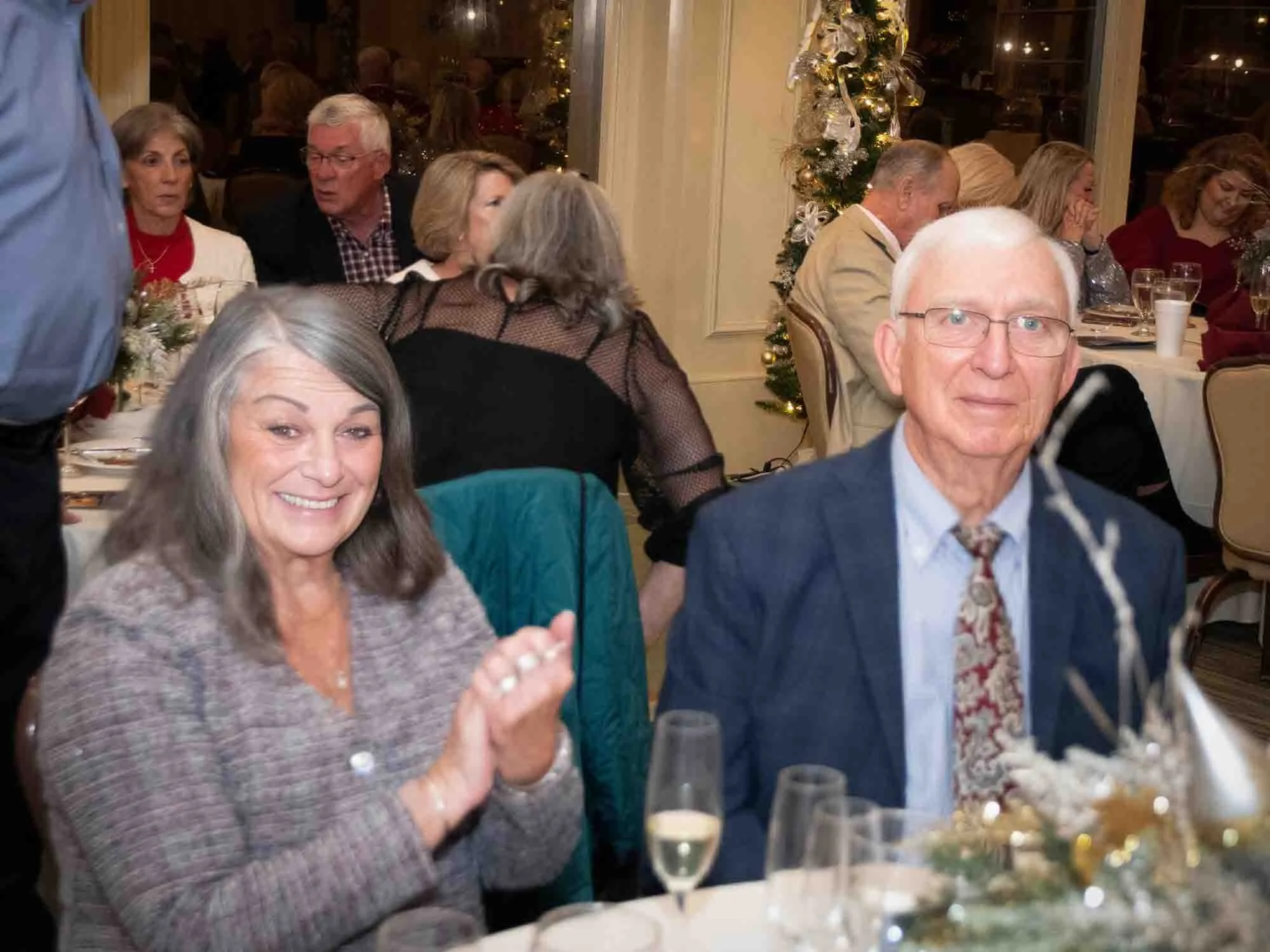 People attending a festive gathering at a decorated venue, with some clapping and others conversing.