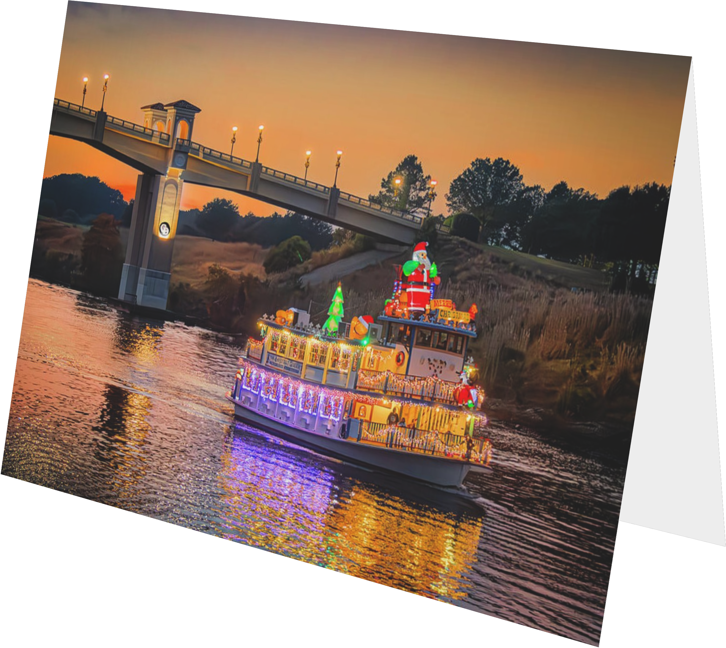 A boat decorated with colorful Christmas lights and holiday figures, including a Santa Claus on the roof, sailing on a river at sunset with a bridge and trees in the background.