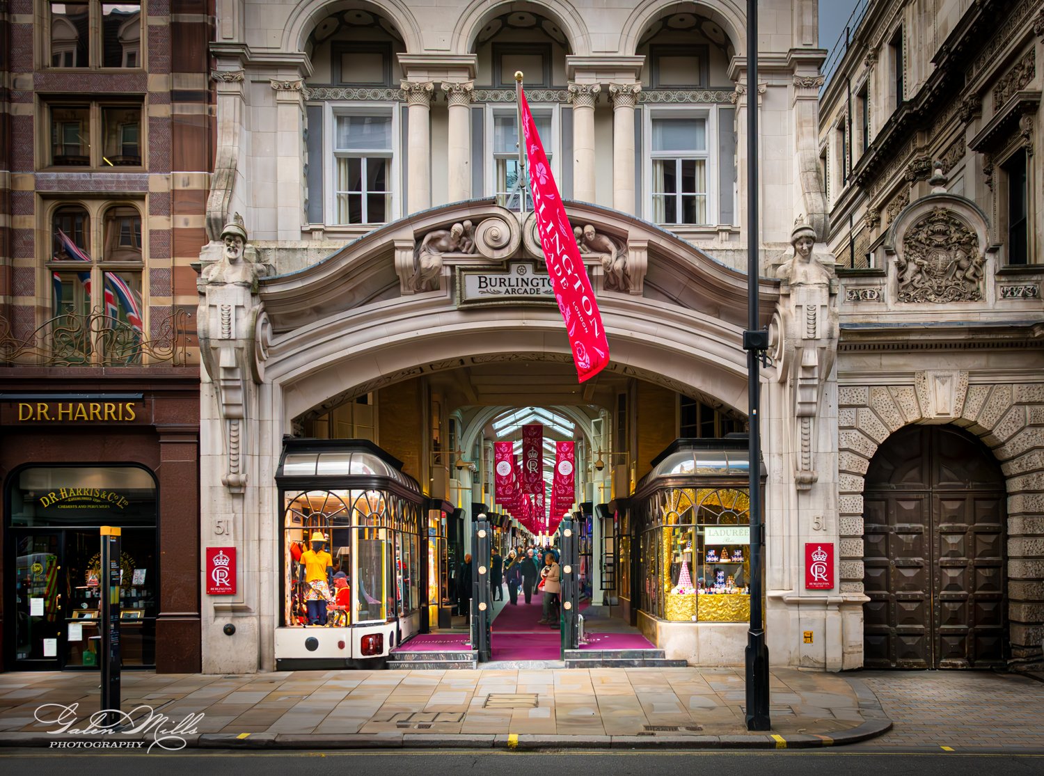 Entrance to Burlington Arcade in London with red flags and elegant architecture.