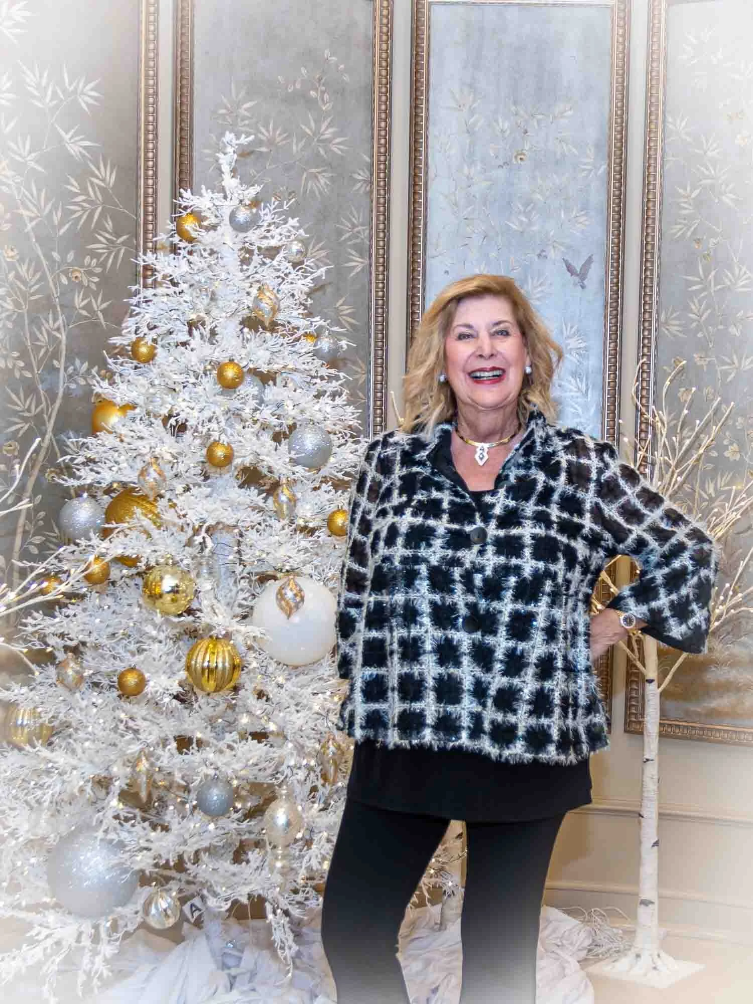 Woman standing beside a white Christmas tree decorated with gold and silver ornaments.