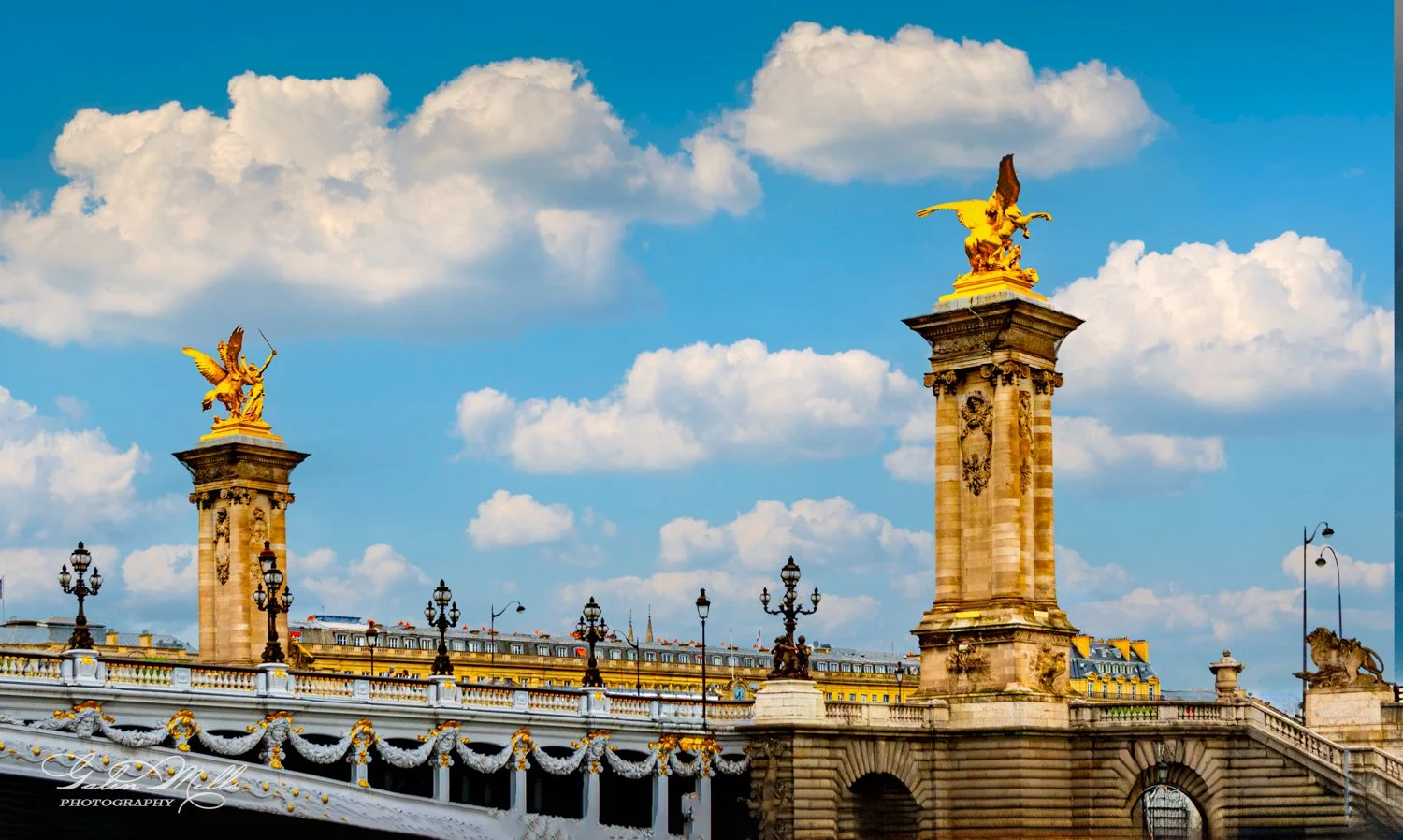 Ornate bridge with golden statues and decorative details against a cloudy blue sky.