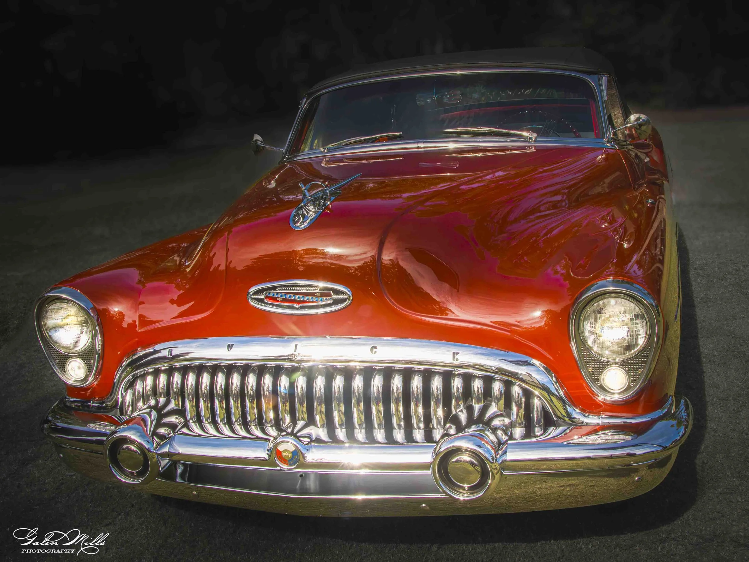 Front view of a shiny red vintage car with a chrome grille and bumper, parked outdoors during daytime.