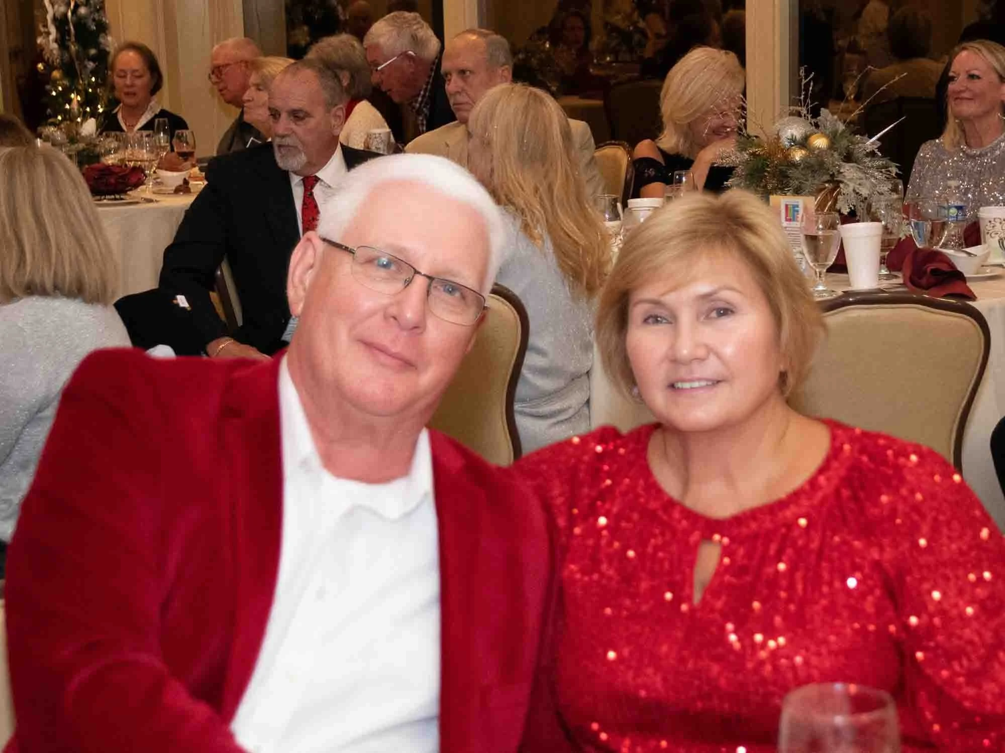 Couple in red outfits at a formal event with seated guests in the background.