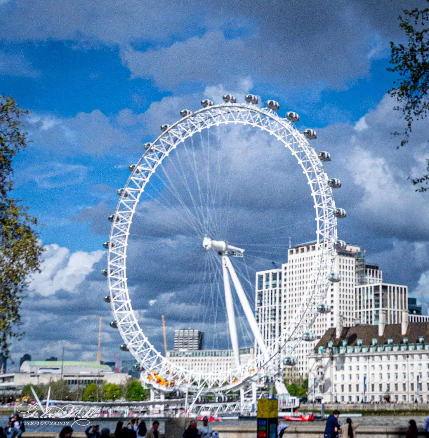 The London Eye, a large Ferris wheel on the South Bank of the River Thames, with a cloudy sky and surrounding buildings.
