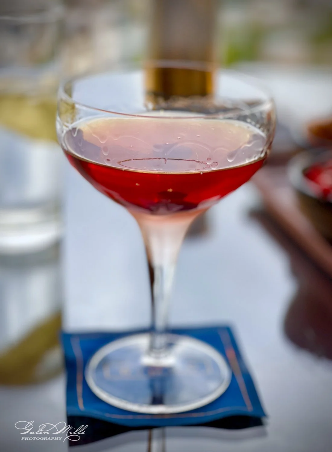 A glass of red cocktail placed on a blue coaster on a table.