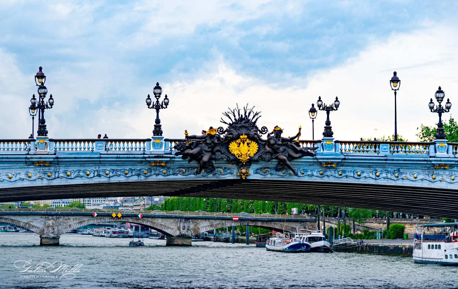 Ornate bridge with sculptures and street lamps, river below, cloudy sky above.