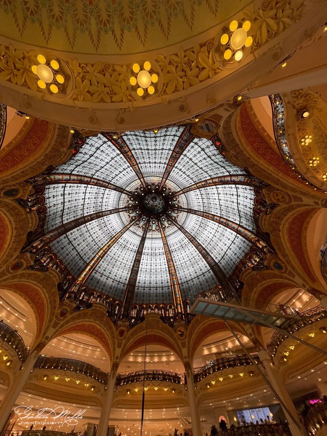 Interior of a shopping mall with a large, ornate glass dome ceiling and decorative arches.