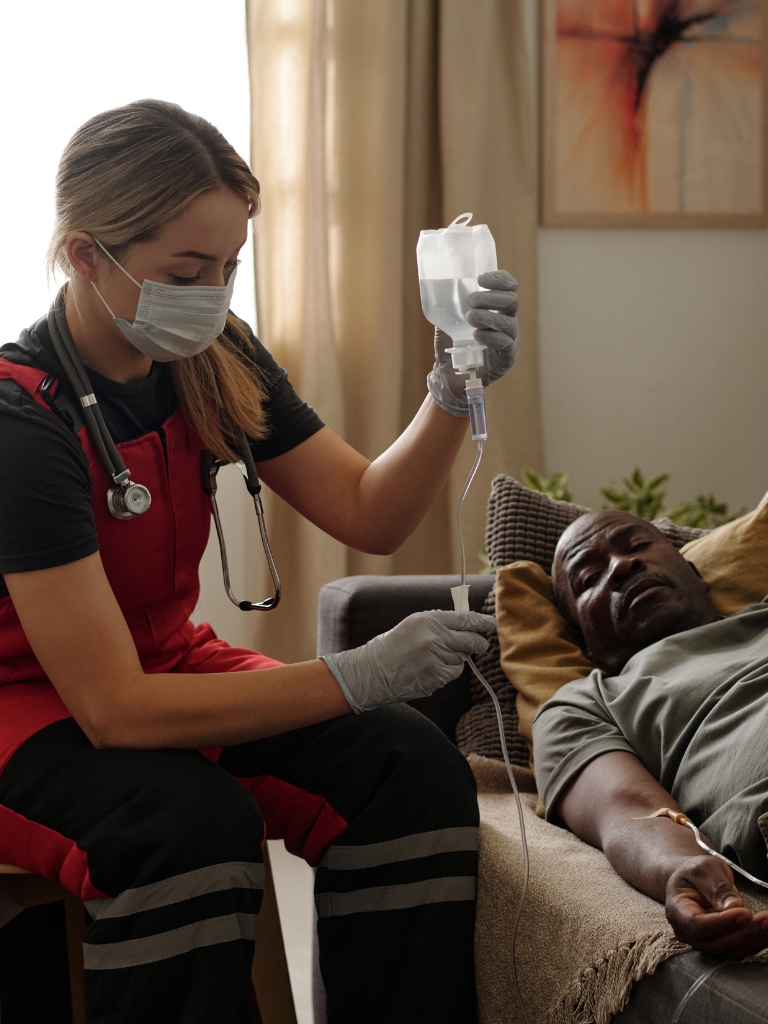 A nurse administering an IV to a man lying on a couch in a living room.