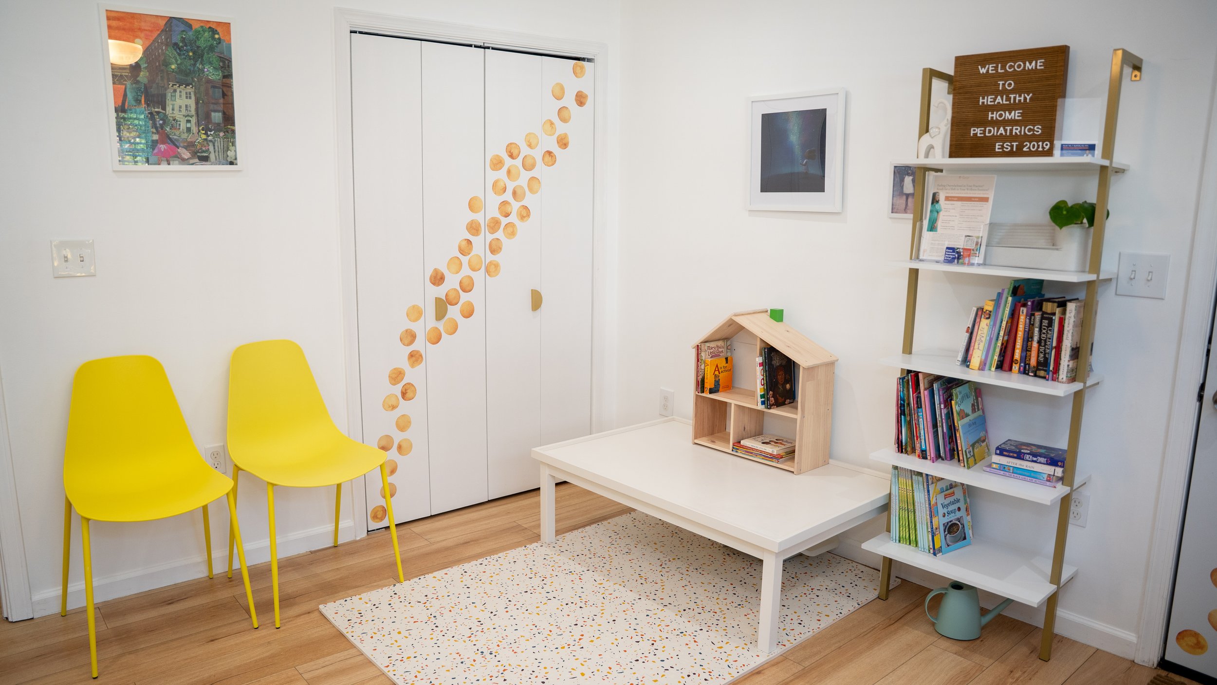 This is a picture of the consultation space and closet. There is a play table and mat. There is a bookshelf with books for children and teens.