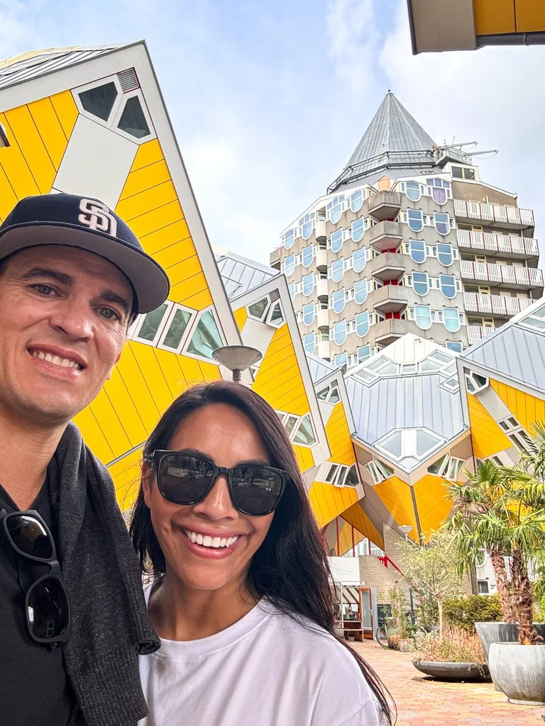 Two people taking a selfie outside of the Seattle Cube Houses with a tall building in the background.
