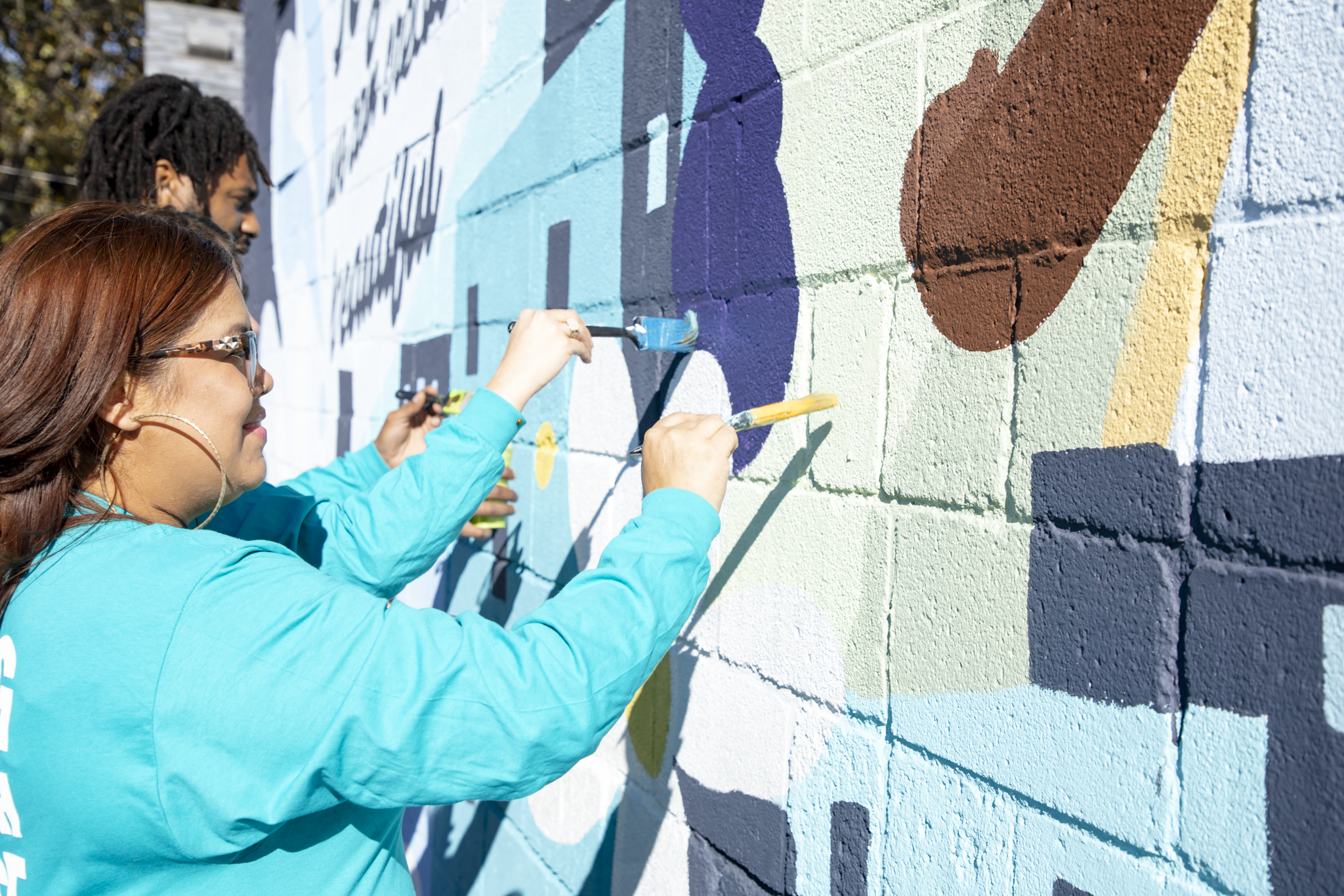People painting a colorful mural on a brick wall outdoors.