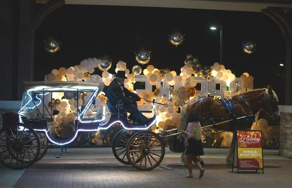 Horse-drawn carriage with string lights surrounded by balloons at night