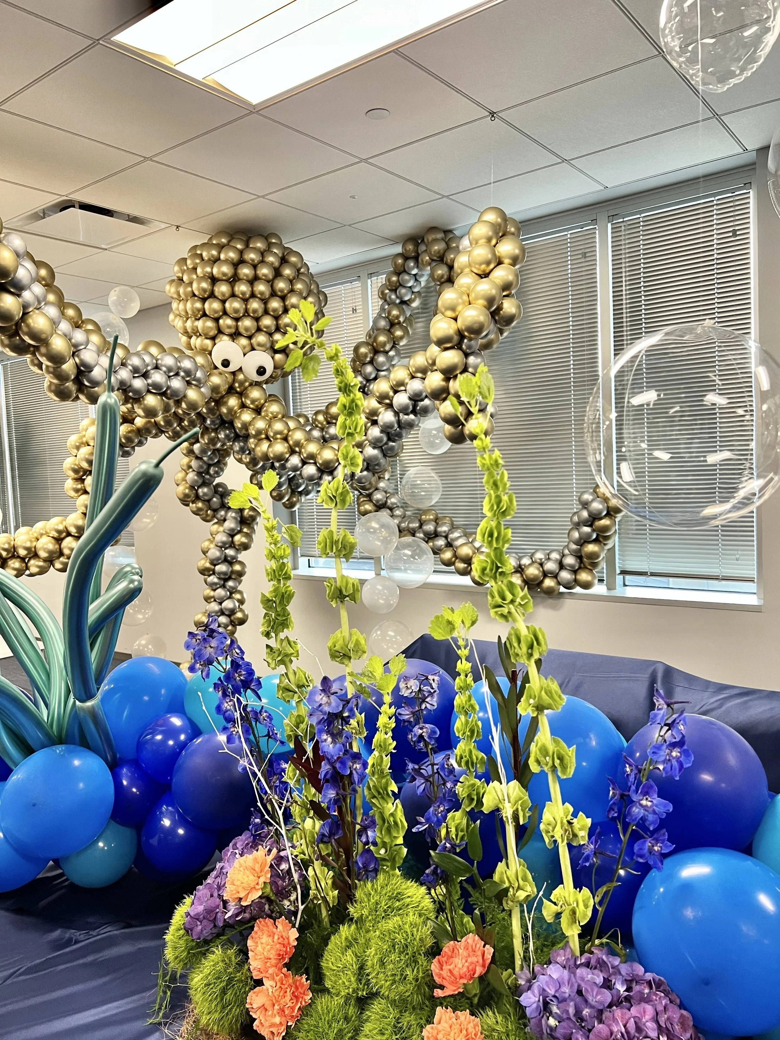 Gold and chrome balloon sculpture above blue florals in a corporate lobby, The Woodlands