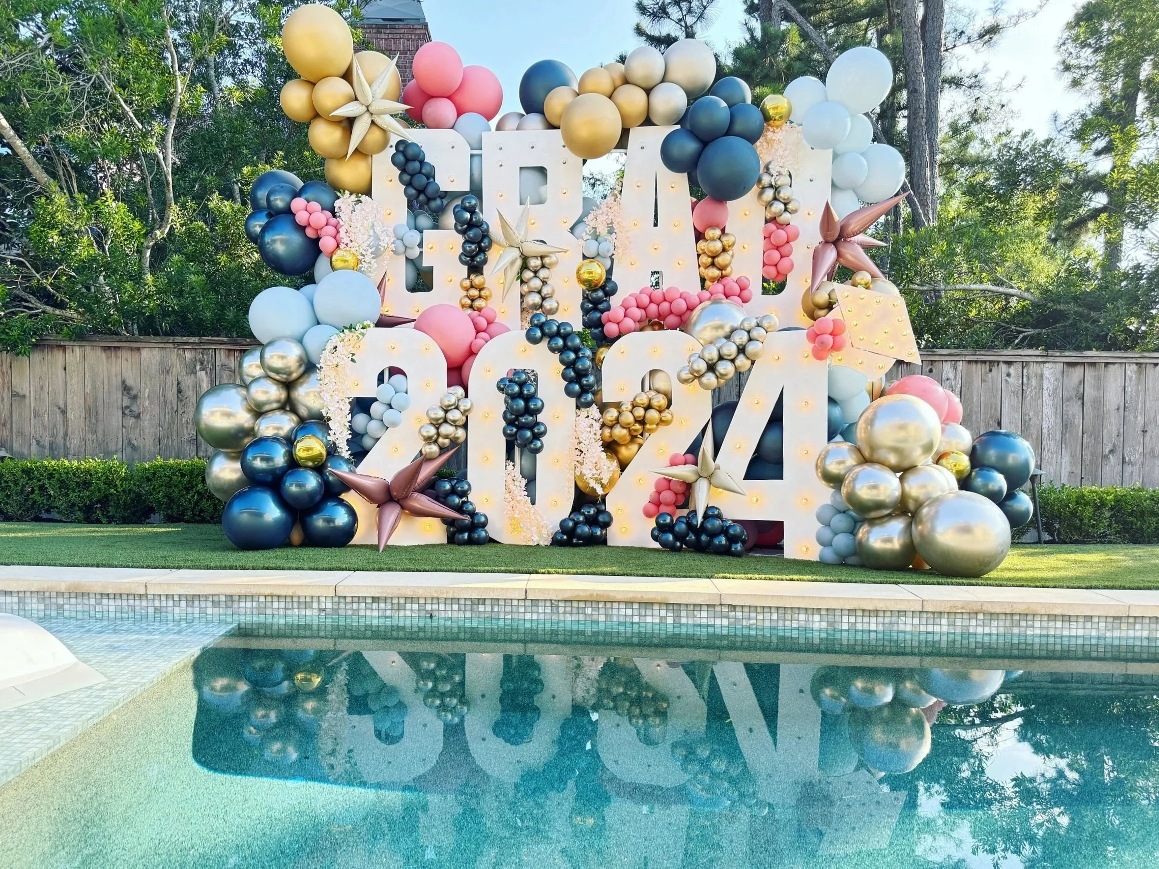 GRAD 2024 marquee letters with navy and gold garland poolside, The Woodlands
