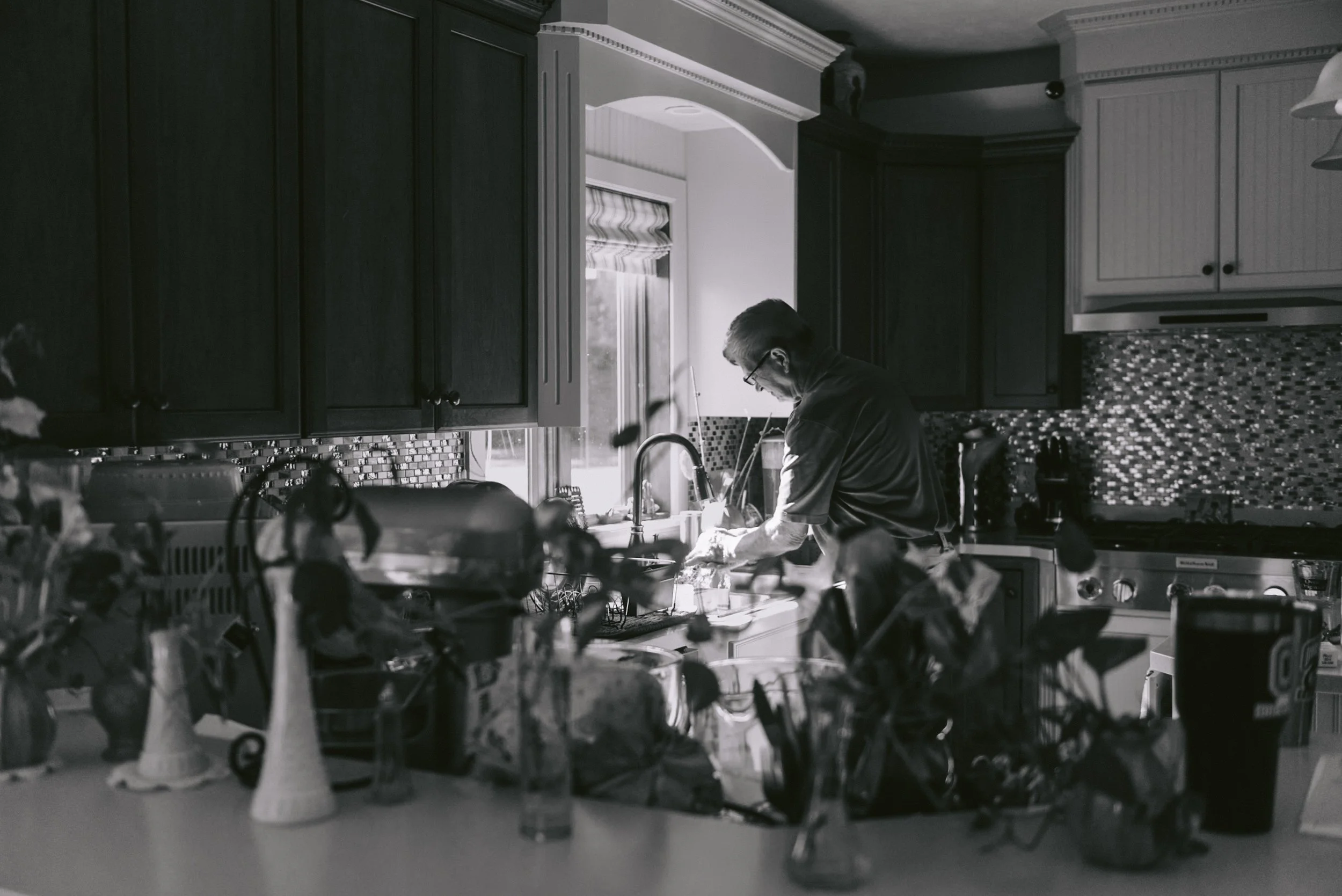 A man washing dishes at the kitchen sink in a well-lit kitchen.