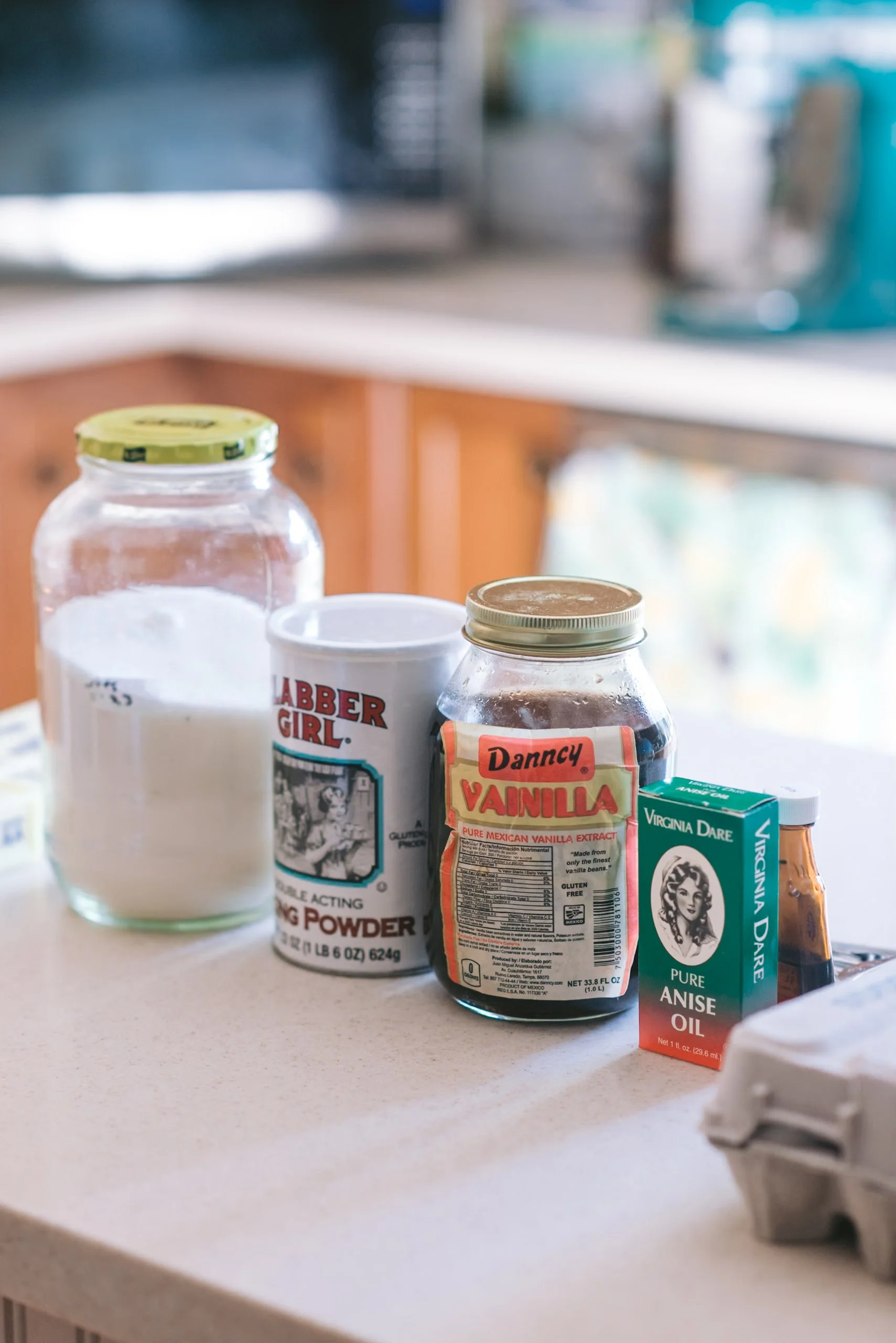 Assorted baking ingredients on a kitchen counter, including a jar of flour, a container of baking powder, vanilla extract, and anise oil.