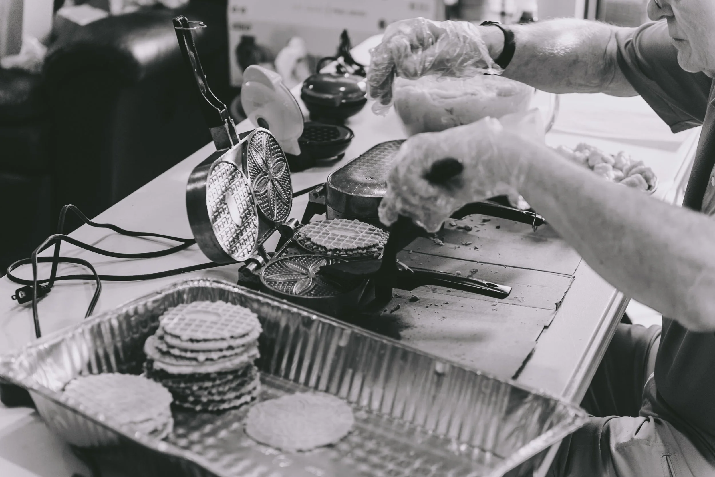 Person making waffles using a waffle iron, with finished waffles in a tray nearby.