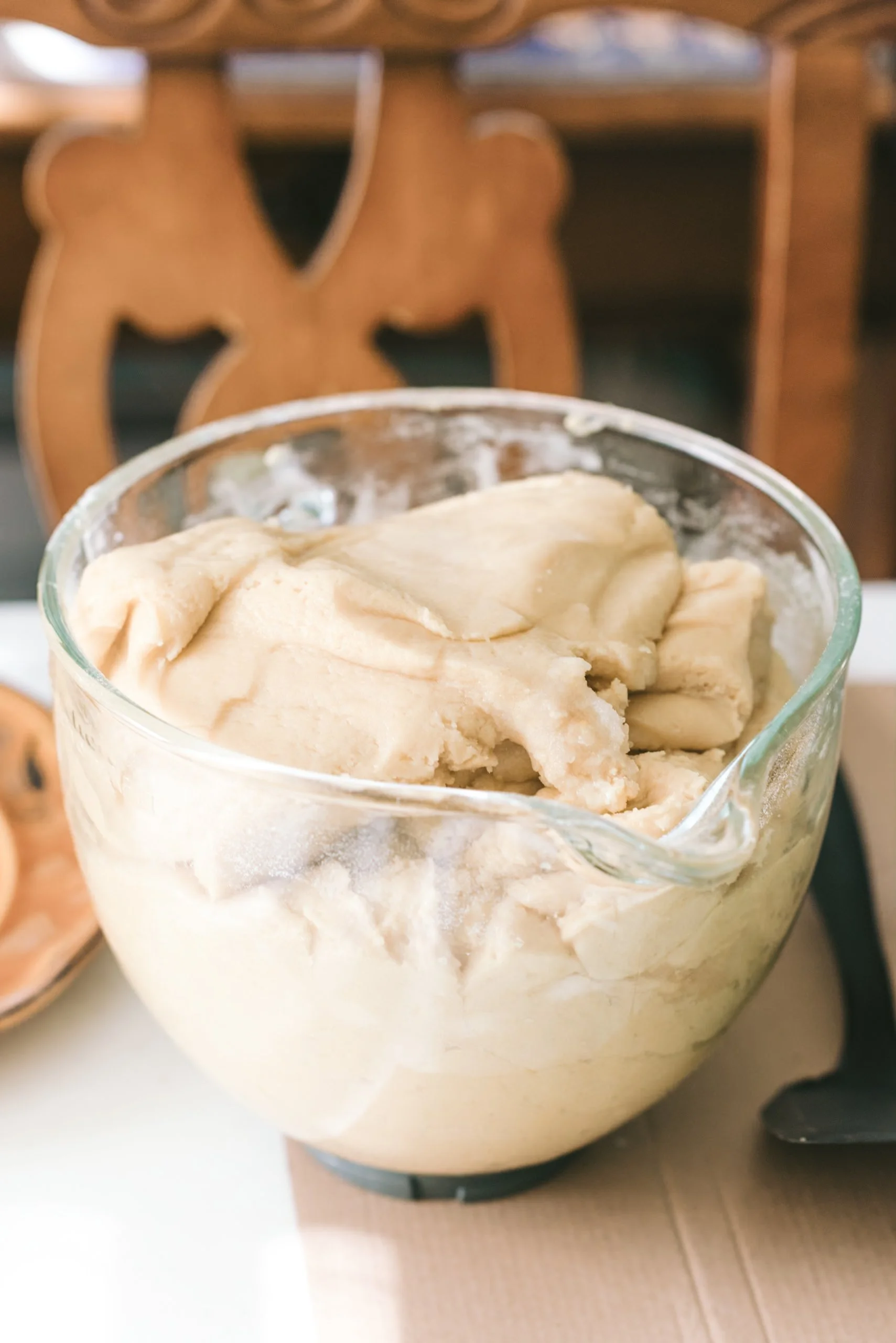 A large glass bowl of homemade vanilla ice cream on a table with a wooden chair in the background.
