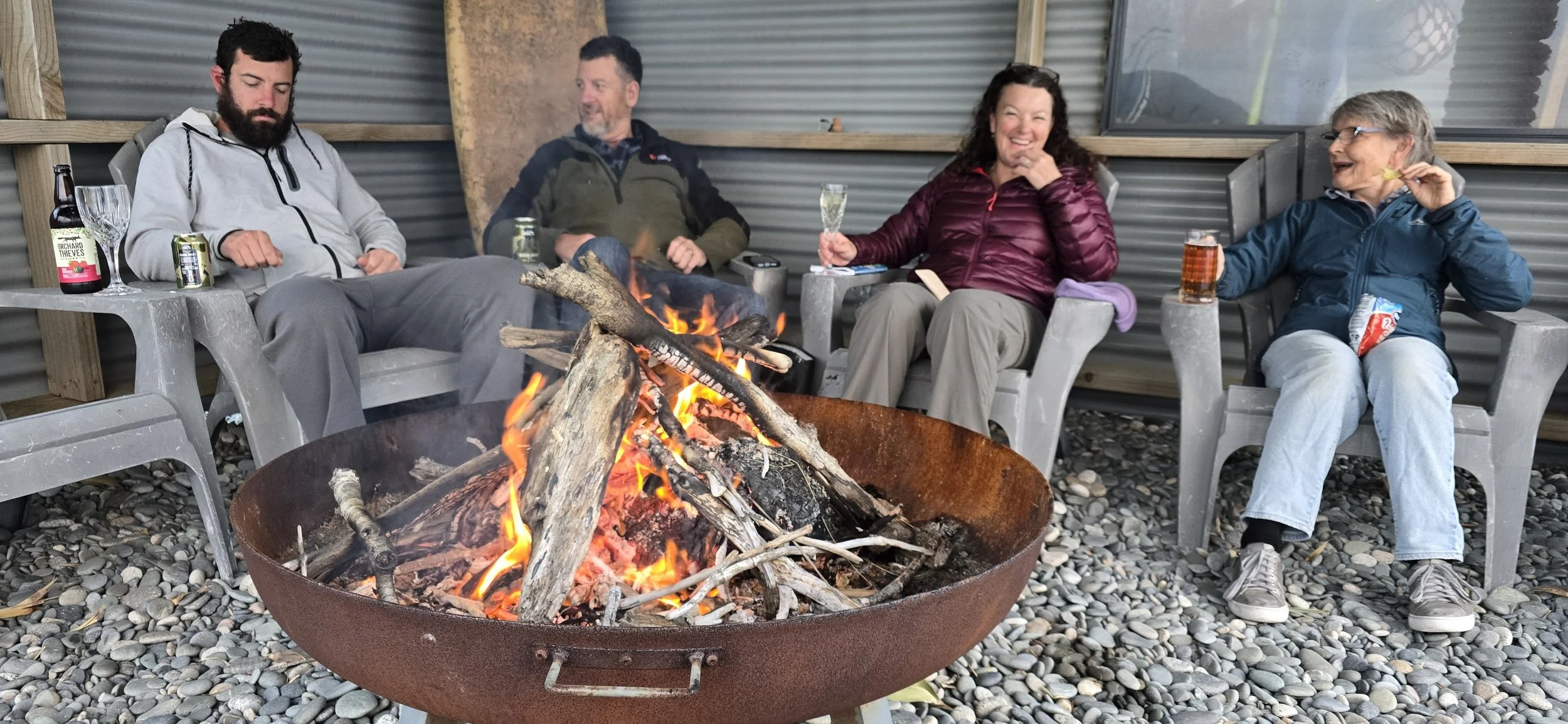 Four people sitting around a campfire on a covered patio, enjoying drinks and conversation.