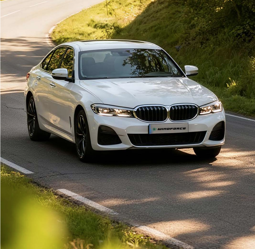 A white BMW sedan driving on a winding road surrounded by green trees and grass.