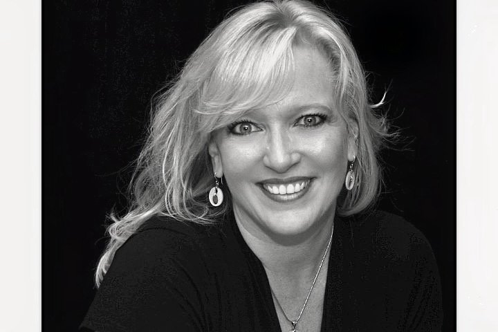 Black and white portrait of a woman with shoulder-length wavy hair, smiling, wearing earrings and a necklace.