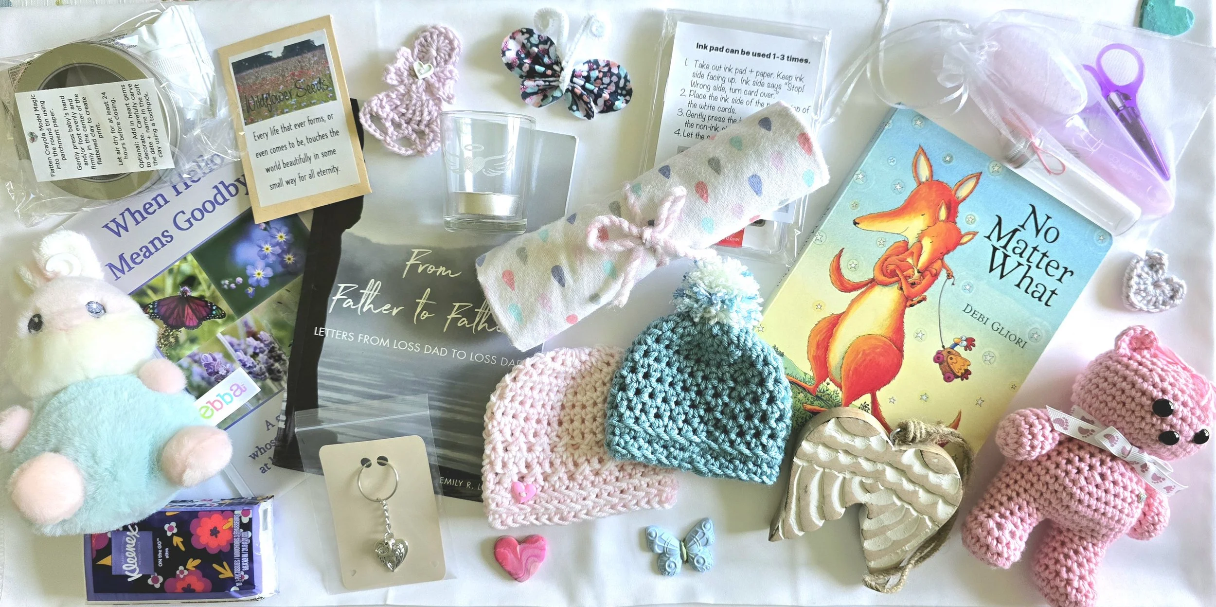 Assorted small gifts and items including crocheted animals, books, a butterfly clip, a candle, and decorative hearts on a white surface.