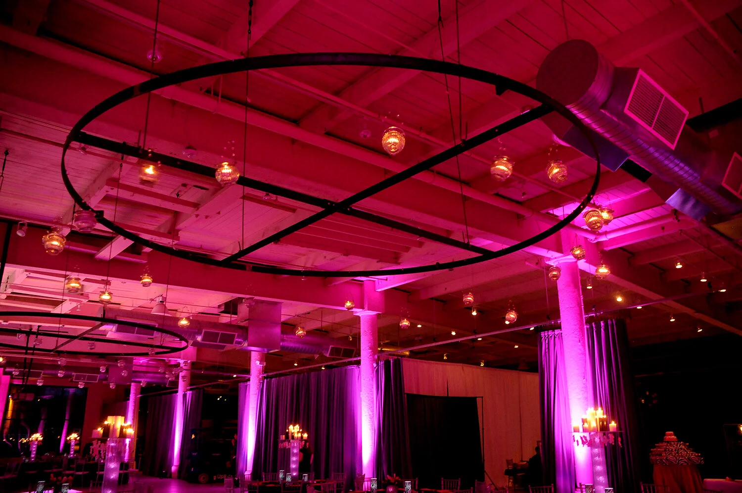Event venue with dramatic pink lighting, large circular decor hanging from the ceiling, and draped curtains.