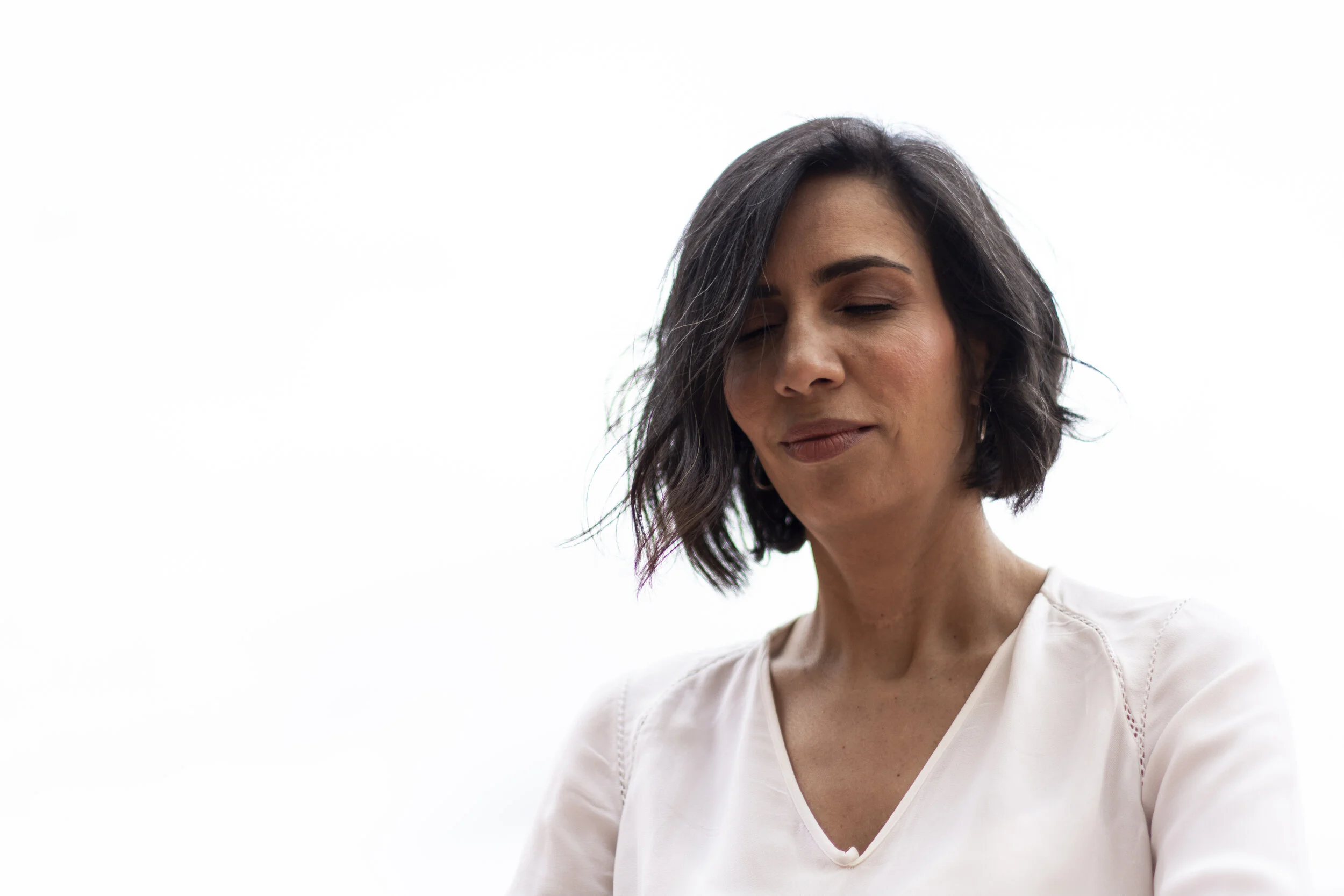 Mujer de cabello oscuro y corto con expresión serena, vestida con blusa blanca, en un fondo blanco