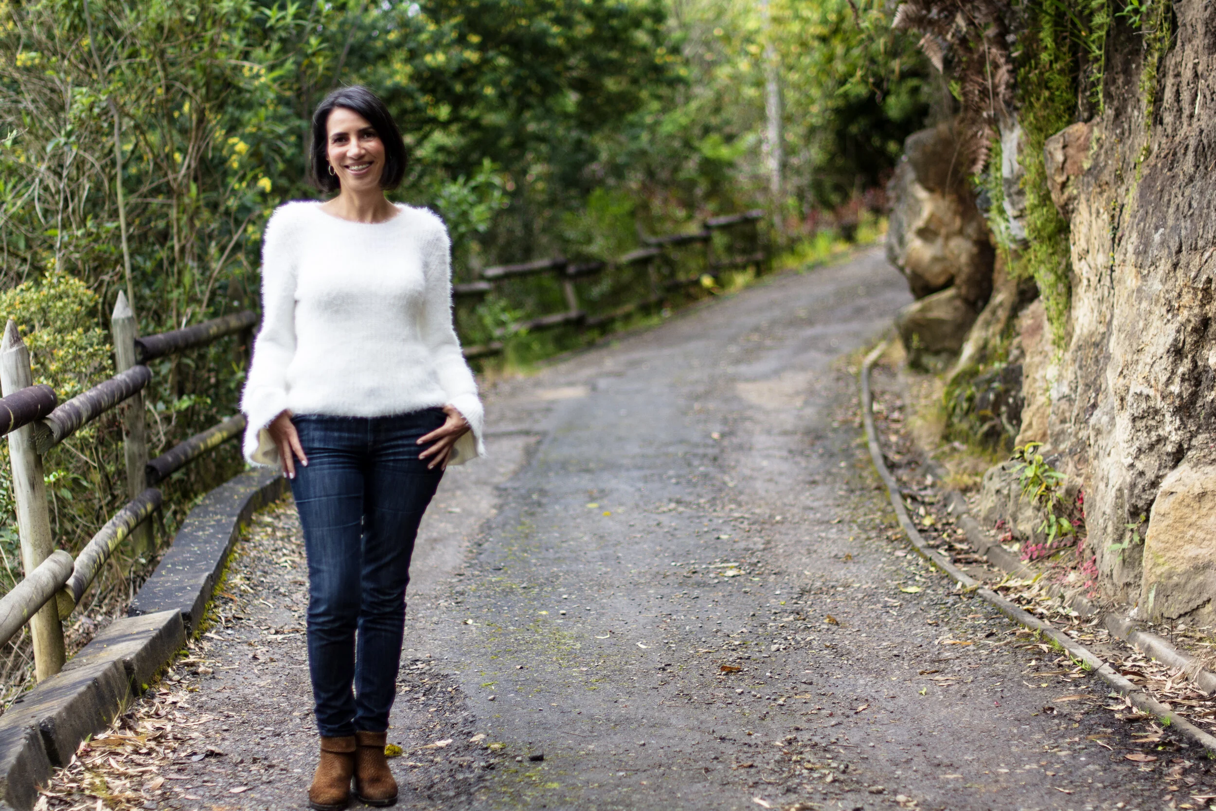 Mujer caminando por un sendero en un bosque con árboles verdes y un borde de madera a un lado.