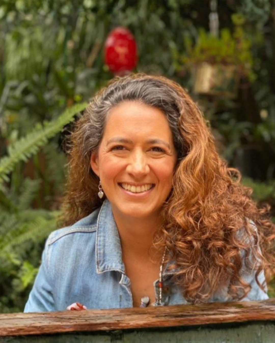 Mujer sonriendo en un entorno natural con vegetación y plantas verdes.