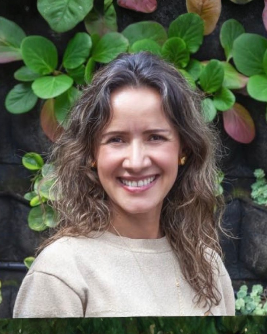 Retrato de una mujer sonriendo con fondo de hojas verdes.