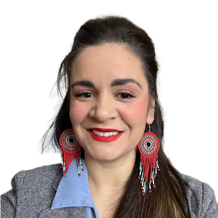 A woman with dark hair, wearing large beaded earrings with red and turquoise patterns, a gray blazer, and a light blue shirt, smiling against a white background.