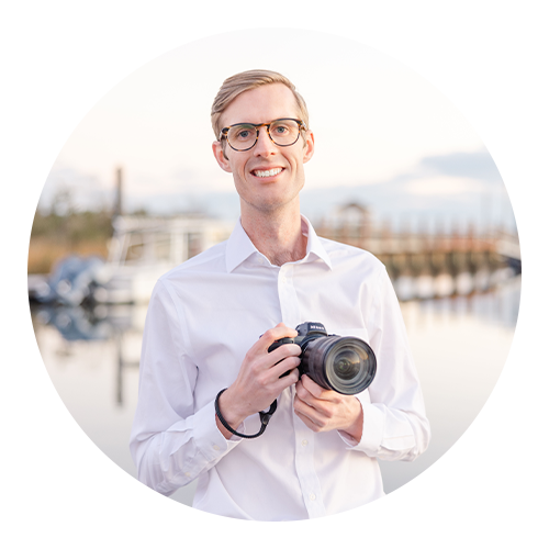 Professional headshot of Andrew Miller, owner of AEM Creative Photography, holding a camera near the marina in Southport, NC, specializing in family, wedding, and coastal photography across Oak Island, Bald Head Island, and Raleigh.