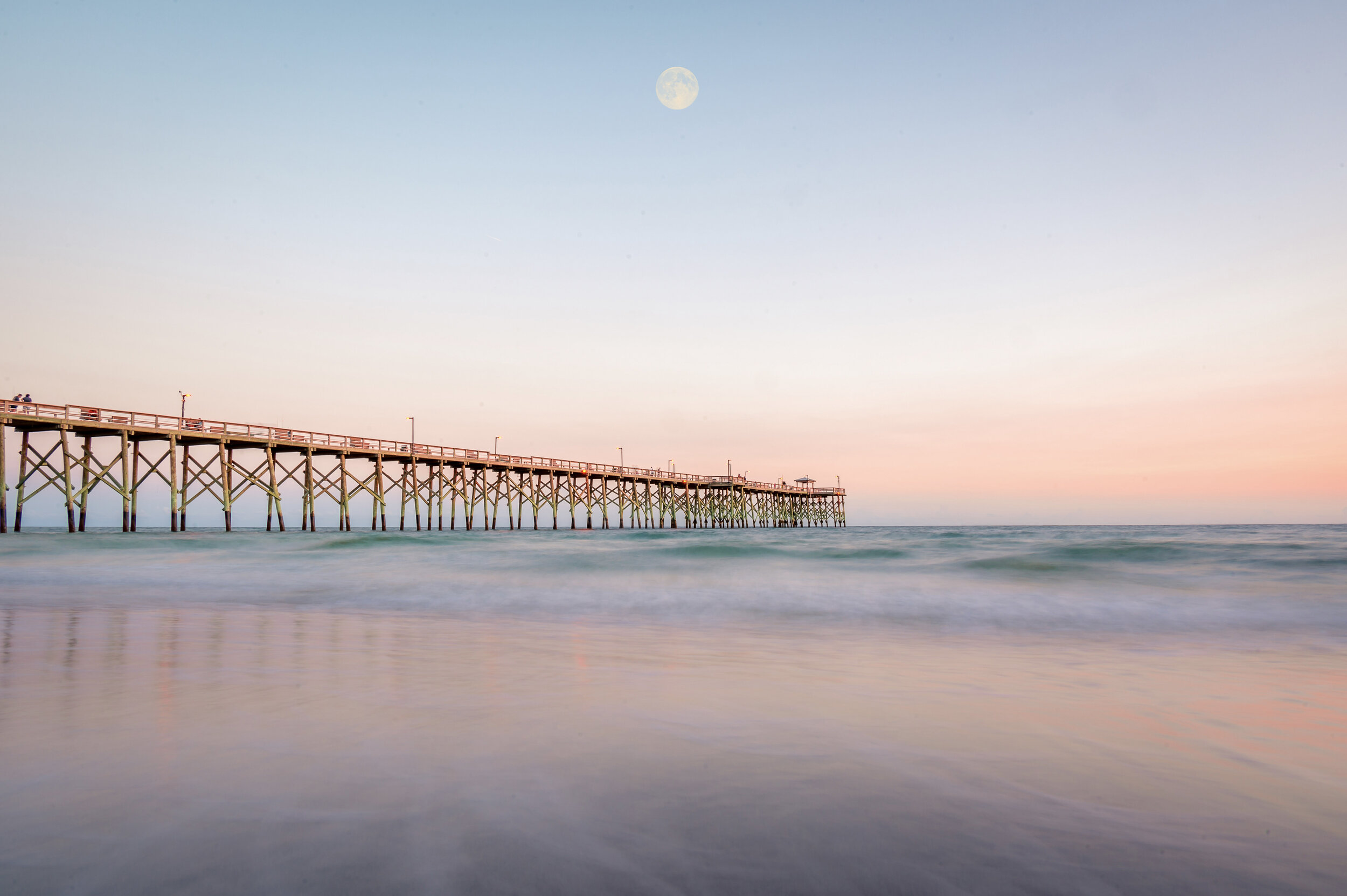 Oak Island Pier extending into the Atlantic Ocean during sunset on Oak Island, North Carolina.