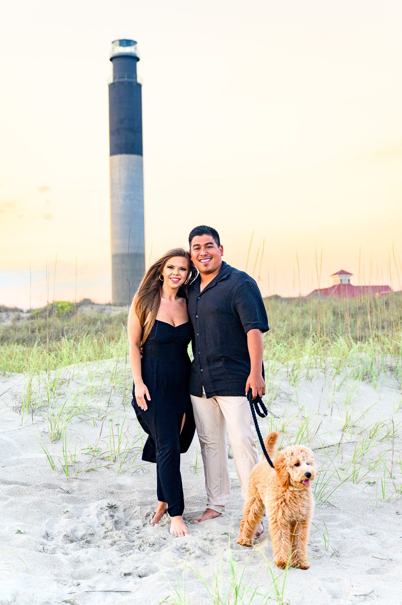 Couple and their dog posing for family photos near the Oak Island Lighthouse at Caswell Beach on Oak Island, North Carolina.